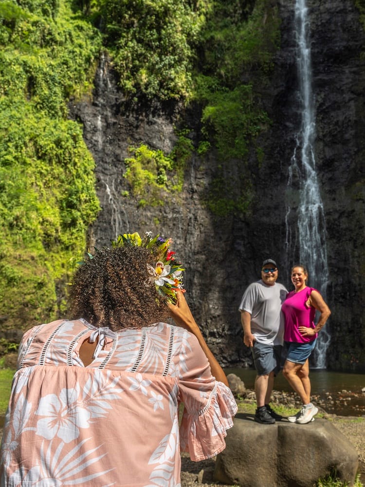 Woman photographing two people posing in front of a tall waterfall